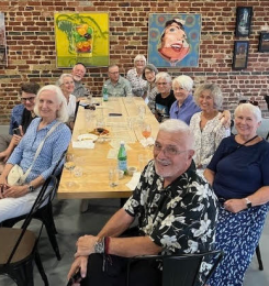 A dozen people sitting around a wooden table; Pieces of art hanging on a brick wall; Building Location:: the Gramophone, 4827 Forest Hill Ave.