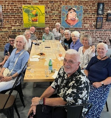 A dozen people sitting around a wooden table; Pieces of art hanging on a brick wall; Building Location:: the Gramophone, 4827 Forest Hill Ave. 