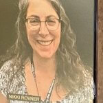 A framed photograph of a smiling person with glasses and long hair, showing nameplates.