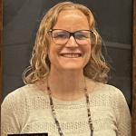 A framed portrait of a person with light hair, glasses, and a white top.