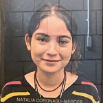 Portrait of a person with a striped black shirt against a tiled background.