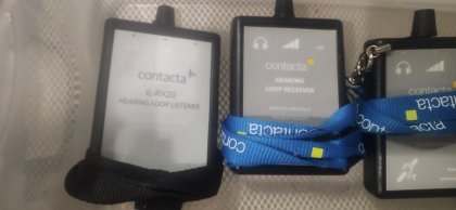 Three black electronic devices with rectangular screens in a container, one with a blue lanyard.