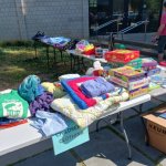Outdoor garage sale with tables displaying children's clothing and board games.